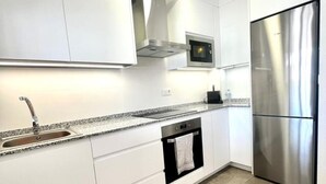 Een moderne keuken met witte kasten, een roestvrijstalen koelkast, een magnetron en een inbouwoven.