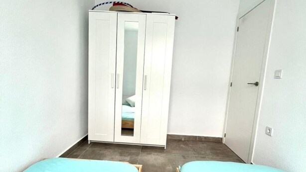 Een slaapkamer met twee eenpersoonsbedden, een witte kast en een deur.