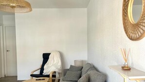 Een moderne woonkamer met een grijze bank, een houten stoel, een ronde houten tafel, een hanglamp en een spiegel aan de muur.