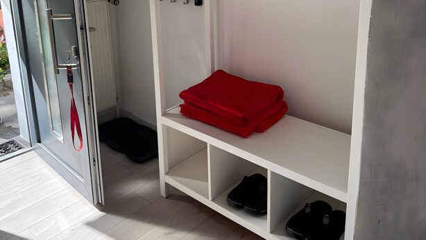 A room with a white wardrobe, a red folded item on the top shelf, a black item on the bottom shelf, and a door with a red strap. - Apartment 'Ferienwohnung Rothentor2' with Private Terrace and Wi-Fi (Dorf Mecklenburg)