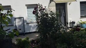 A white building with a door, windows, and a small garden area with plants and flowers. - Apartment 'Ferienwohnung Rothentor2' with Private Terrace and Wi-Fi (Dorf Mecklenburg)