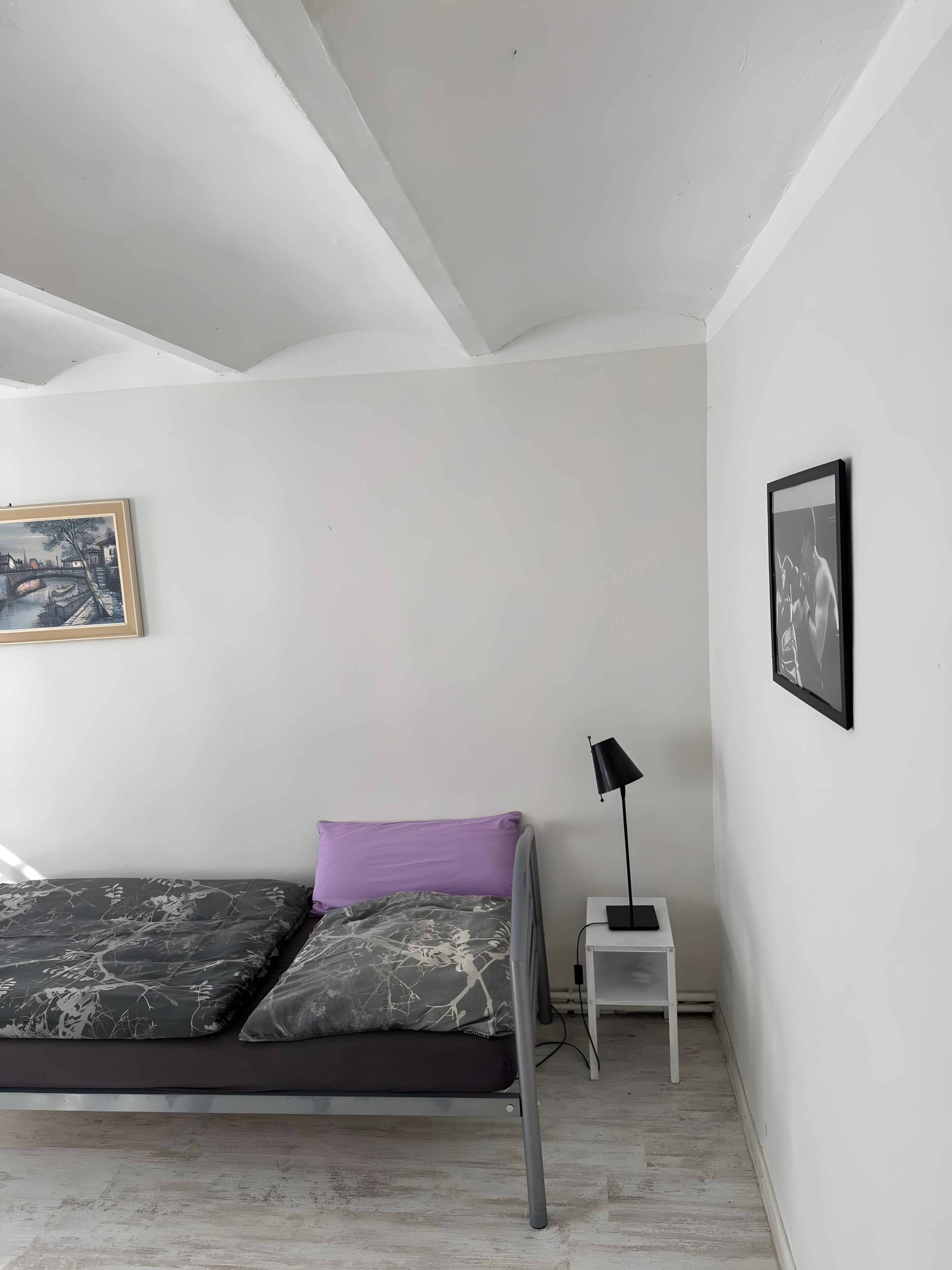 Ein Schlafzimmer mit einem Bett, einem Nachttisch, einer Lampe und zwei gerahmten Bildern an der Wand.