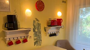 A room with a table, two chairs, a clock, a coffee maker, a toaster, and a window with a view. - Apartment 'Ferienwohnung Rothentor2' with Private Terrace and Wi-Fi (Dorf Mecklenburg)