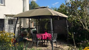 A covered patio with a table and chairs, surrounded by greenery and a house in the background. - Apartment 'Ferienwohnung Rothentor2' with Private Terrace and Wi-Fi (Dorf Mecklenburg)