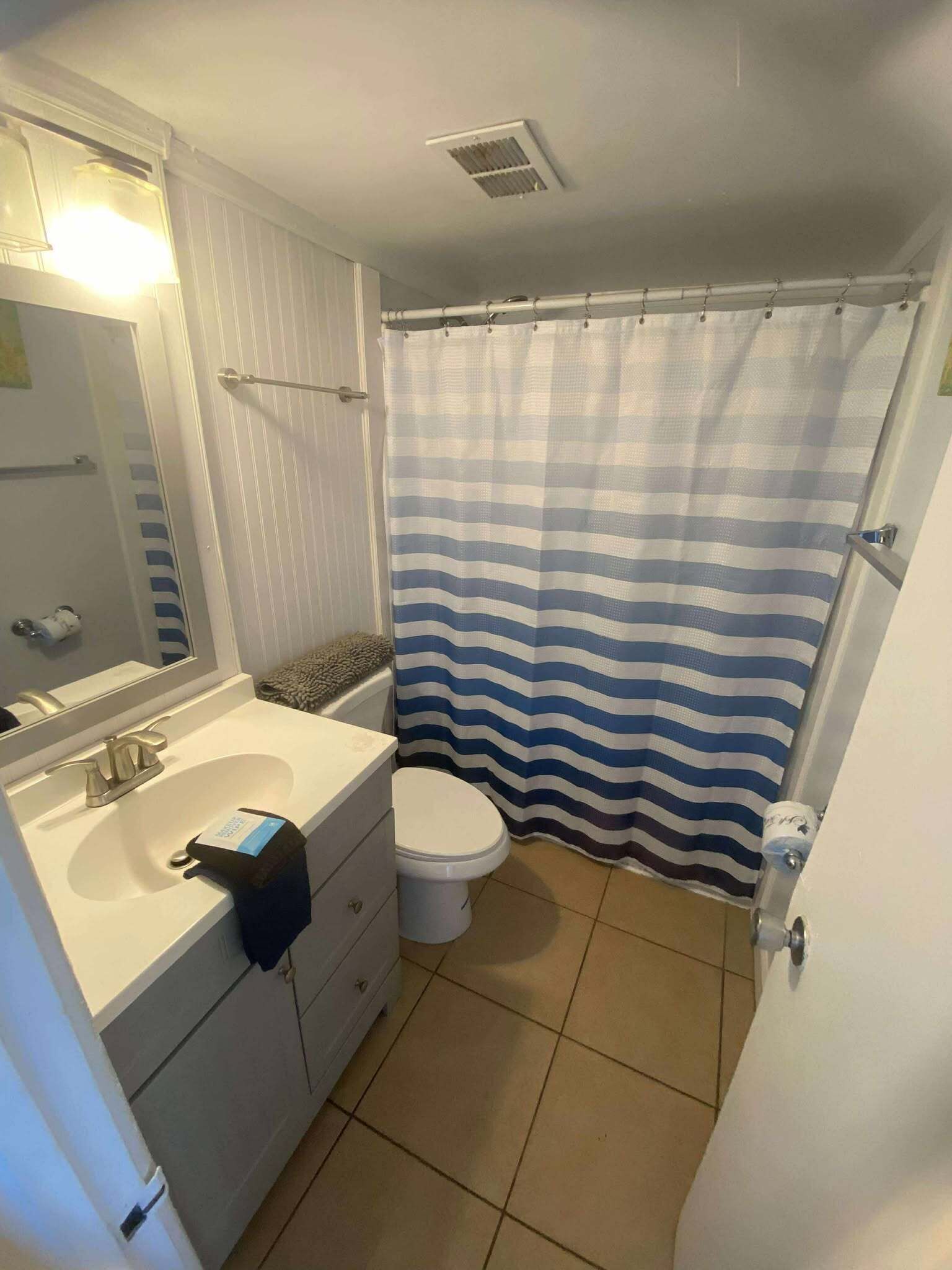Een badkamer met een wit wastafelmeubel, een spiegel, een toilet en een douchegordijn met strepen.