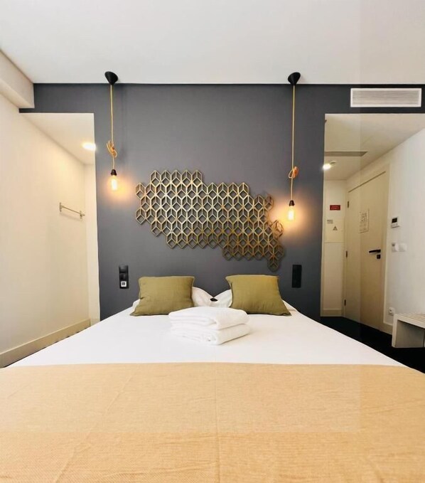 A hotel room with a bed, two bedside lamps, a geometric wall decoration, and a door to the right. - Villa Rossio (Aveiro)