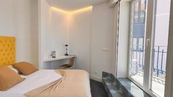 A modern hotel room with a large bed, a desk, and a window with a balcony view.