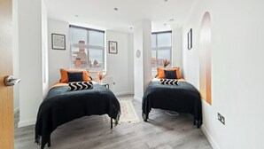 A modern bedroom with two beds, large windows, and a view of buildings outside. - The Copper Nest 2BR City Centre (Leicester)