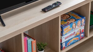 A television with the Netflix logo on the screen, a remote control, and a shelf with children's books and toys. - The Copper Nest 2BR City Centre (Leicester)