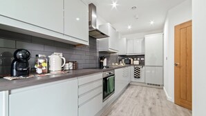 A modern kitchen with white cabinets, a dark countertop, and a built-in oven. - The Copper Nest 2BR City Centre (Leicester)