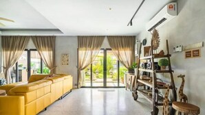 Una sala de estar moderna con un sofá amarillo, una estantería de madera y un ventanal con cortinas.