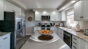 Cozinha moderna com armários brancos, eletrodomésticos de aço inoxidável e uma ilha central com cesta de vime.