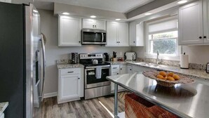 Cocina moderna con armarios blancos, electrodomésticos de acero inoxidable y encimera de granito.