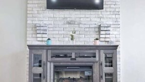 Una sala de estar con un televisor de pantalla plana montado en una pared de ladrillo, una chimenea con puerta de cristal y un mueble de entretenimiento moderno.