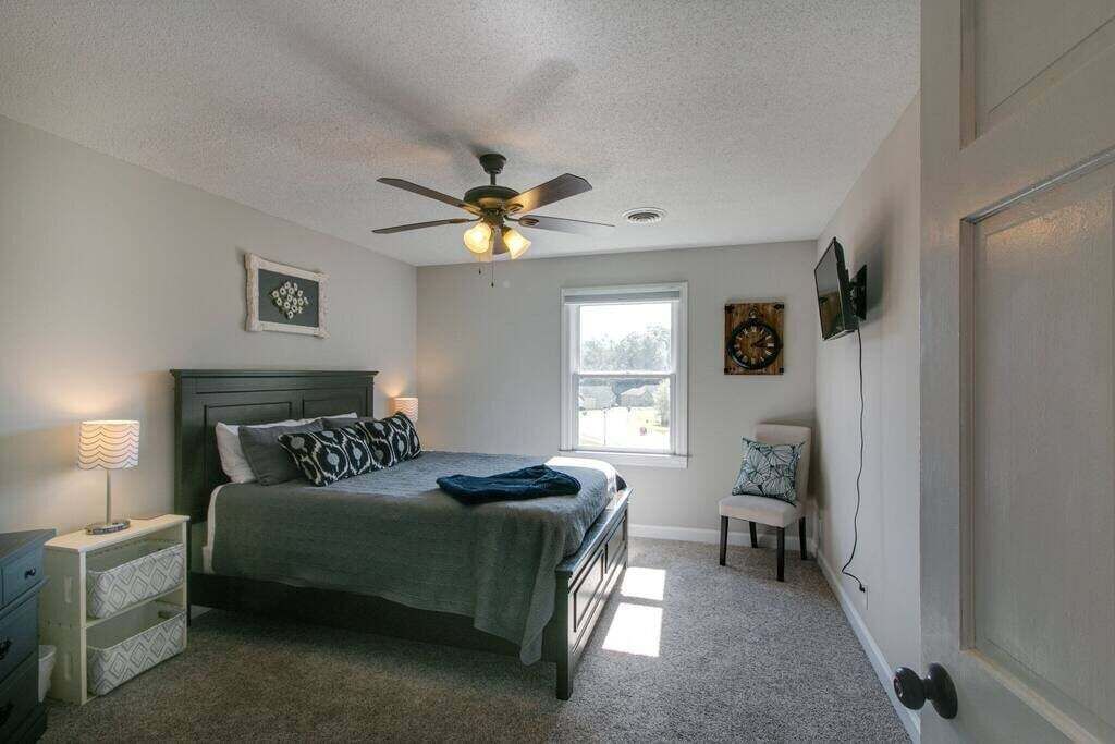 Une chambre à coucher avec un lit, un ventilateur de plafond, une fenêtre, un téléviseur fixé au mur et une porte avec une poignée.