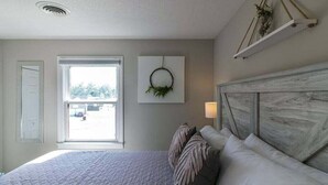 Een slaapkamer met een bed, een raam, een aan de muur bevestigd kransje en een houten hoofdeinde.