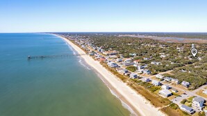 An aerial view of a coastal town with a pier extending into the sea, surrounded by residential buildings and greenery. - Walk to beach access - hot tub, dog friendly, sleeps 9! (Oak Island)