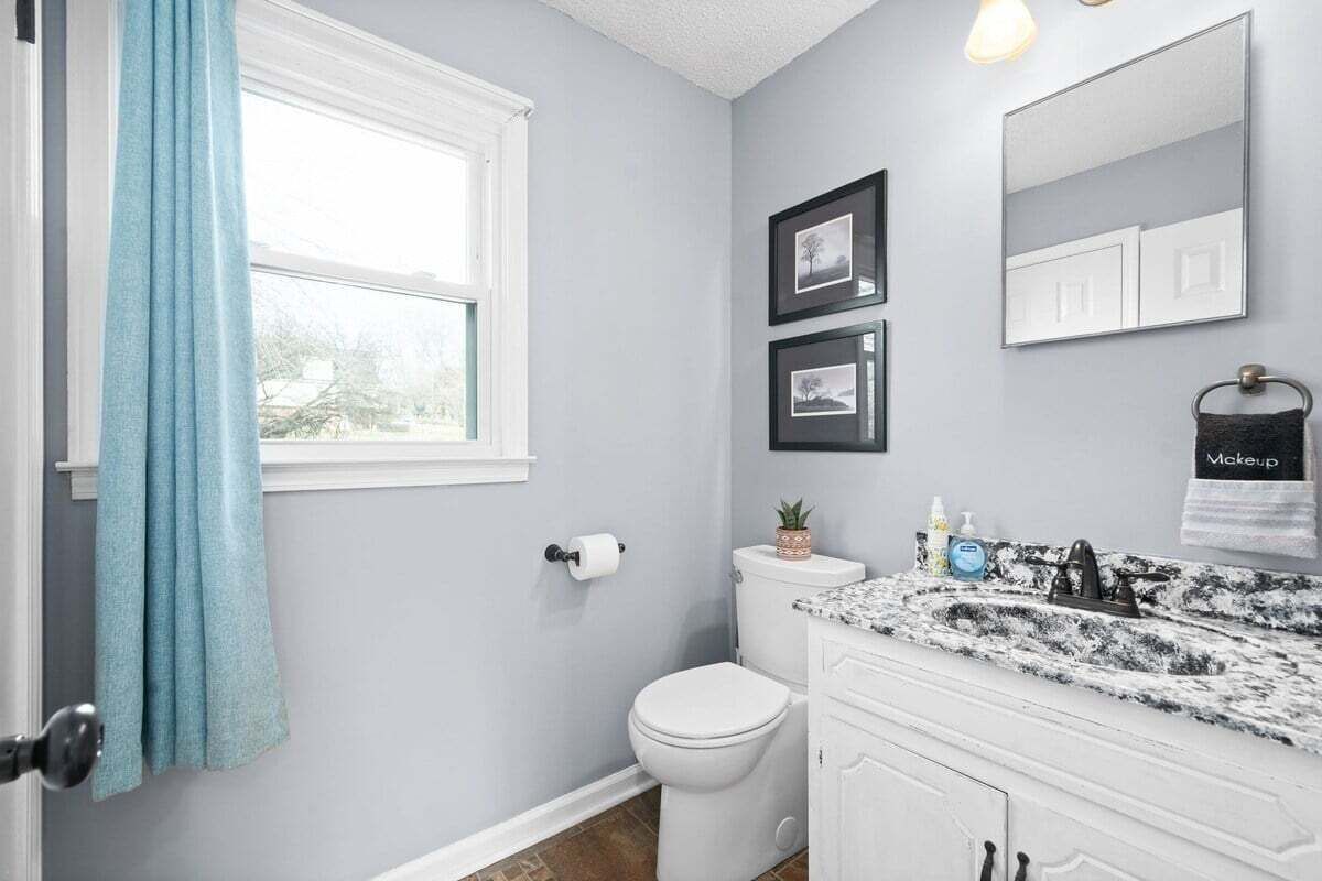 A bathroom with a toilet, sink, and a window with a blue curtain.