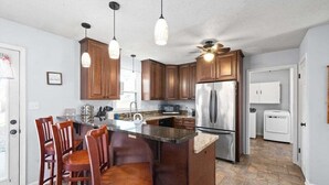 A kitchen with wooden cabinets, a stainless steel refrigerator, and a bar area with stools.