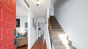 A hallway with a red door, a staircase with carpeted steps, and a beige sofa with a blue cushion.