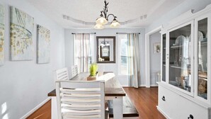 A dining room with a wooden table, white chairs, a chandelier, and a cabinet with glass doors.