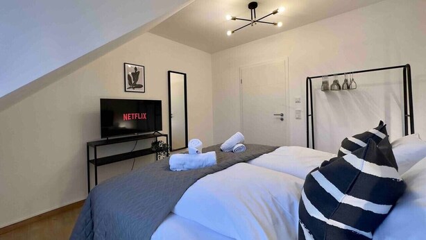 A hotel room with a bed, a TV, a ceiling light, and a door. - Modern apartment with kitchen & parking (Stephansposching)