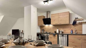 A modern kitchen with wooden cabinets, a built-in oven, and a dining area set for six with a wooden table and six white plates. - Modern apartment with kitchen & parking (Stephansposching)