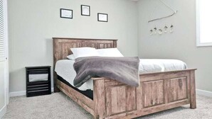A bedroom with a wooden bed, a small bedside table, and a wall-mounted light fixture. - Magnolia Summary:<br>Hil (Clarksville)