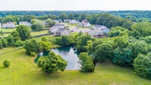 An aerial view of a residential area with houses, a pond, and surrounding greenery. - Magnolia Summary:<br>Hil (Clarksville)