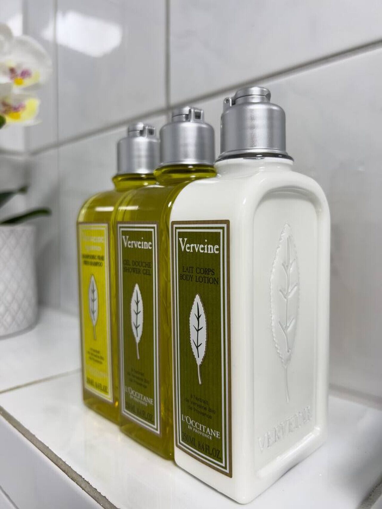 Three bottles of Verveine body lotion on a white shelf.