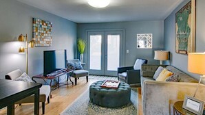 Un salon moderne doté d’un téléviseur, d’un espace salon et d’une grande fenêtre.