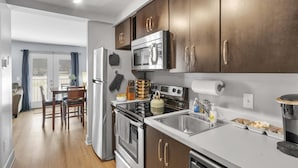 A modern kitchen with stainless steel appliances, wooden cabinets, and a dining area with a table and chairs. - Loft #208 (540 N 2nd St) (Fredericton)