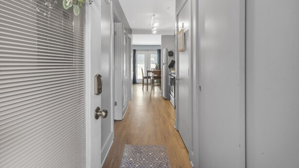 A hallway with a wooden floor, white walls, and a door with a brass handle. - Loft #208 (540 N 2nd St) (Fredericton)