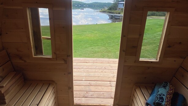 A cabin with a wooden interior, a small wooden bench, and a view of a lake through a window. - 7-bed lakefront house with sauna, beach & boat launch — 15 min from Thunder Bay. (Thunder Bay)
