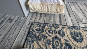 Ett kompakt köksområde med ett kylskåp i rostfritt stål, en vadderad förvaringsbänk och en mönstrad matta på golvet.
