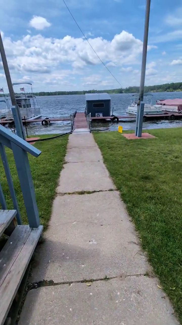 A concrete pathway leading to a dock with boats, a grassy area, and a clear sky.