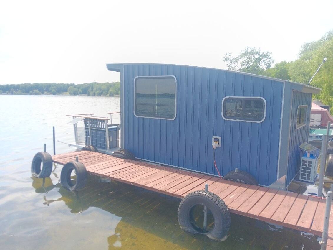 Una cabaña azul pequeña con un muelle de madera que se adentra en un lago.