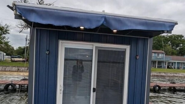 En liten stuga med ett enda rum, med blå fasad och en vit dörr, och en välkomstmatta vid ingången.