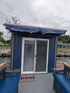 Une petite cabane d’une seule pièce, à l’extérieur bleu et à la porte blanche, avec un paillasson « Bienvenue » devant l’entrée.