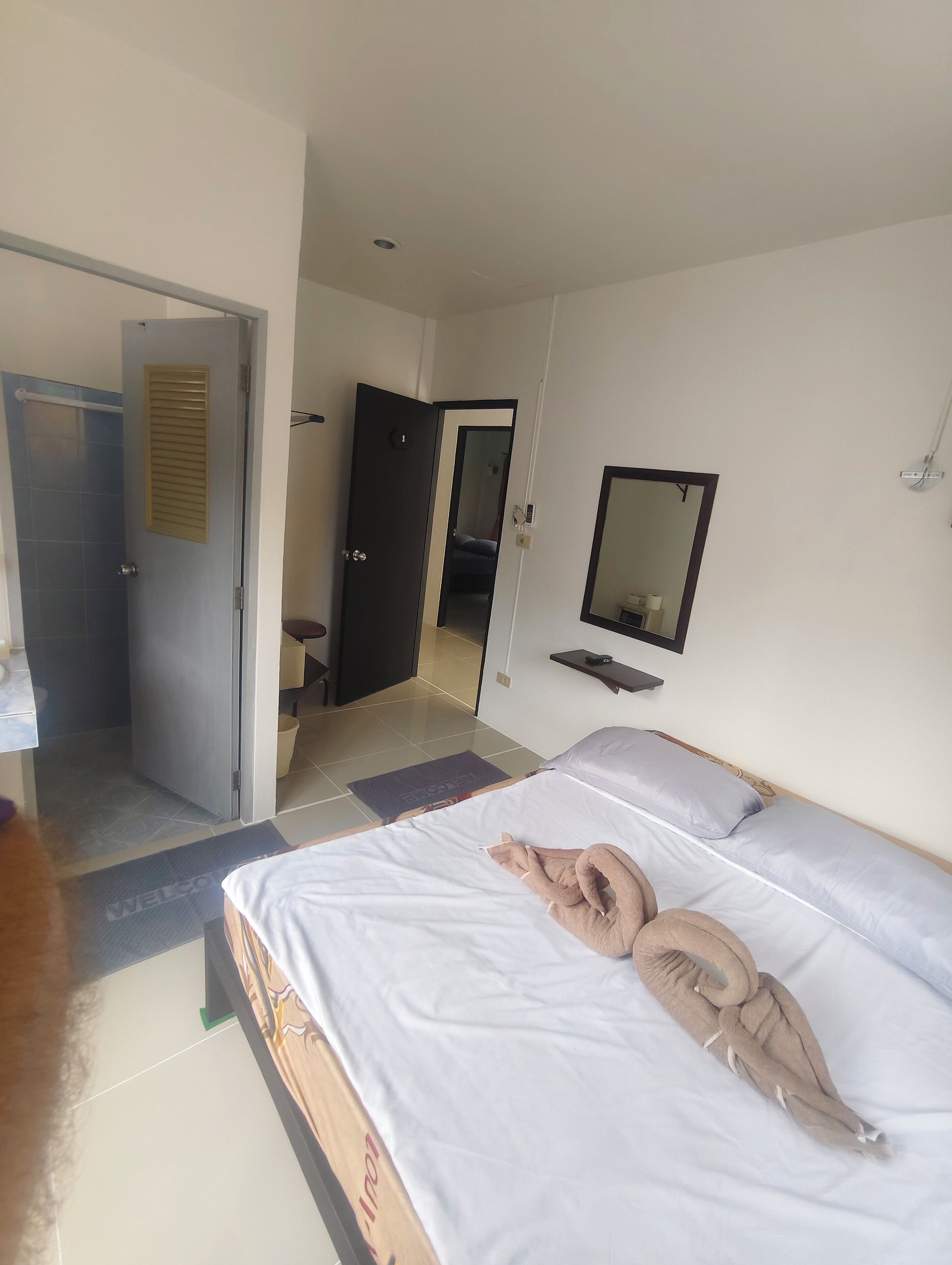 A hotel room with a bed, a bathroom door, a mirror, and a shower area.