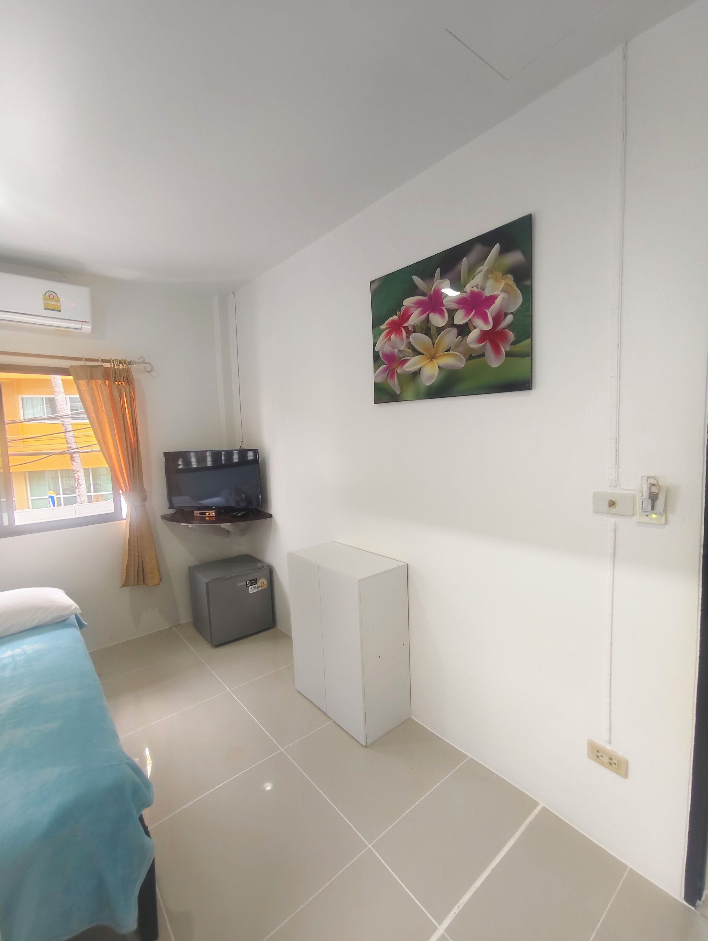 Una habitación con cama, televisor, un mueble pequeño y un cuadro en la pared.