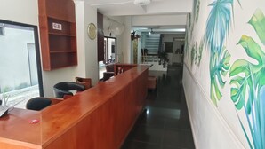 Una reception con una scrivania, un orologio, un cartello che indica divieto di fumo e un murale con piante tropicali.