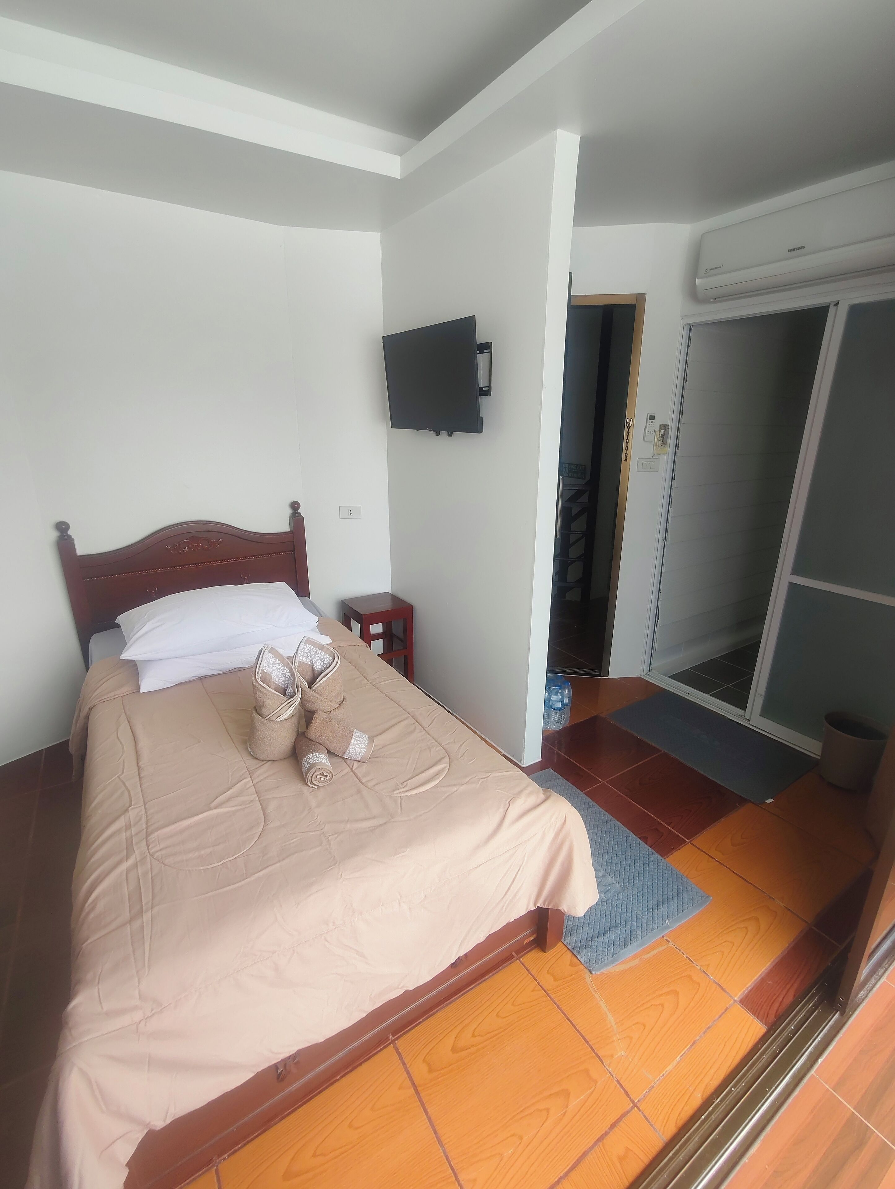 Una habitación de hotel con una cama, un televisor instalado en la pared y un armario con puerta corredera.