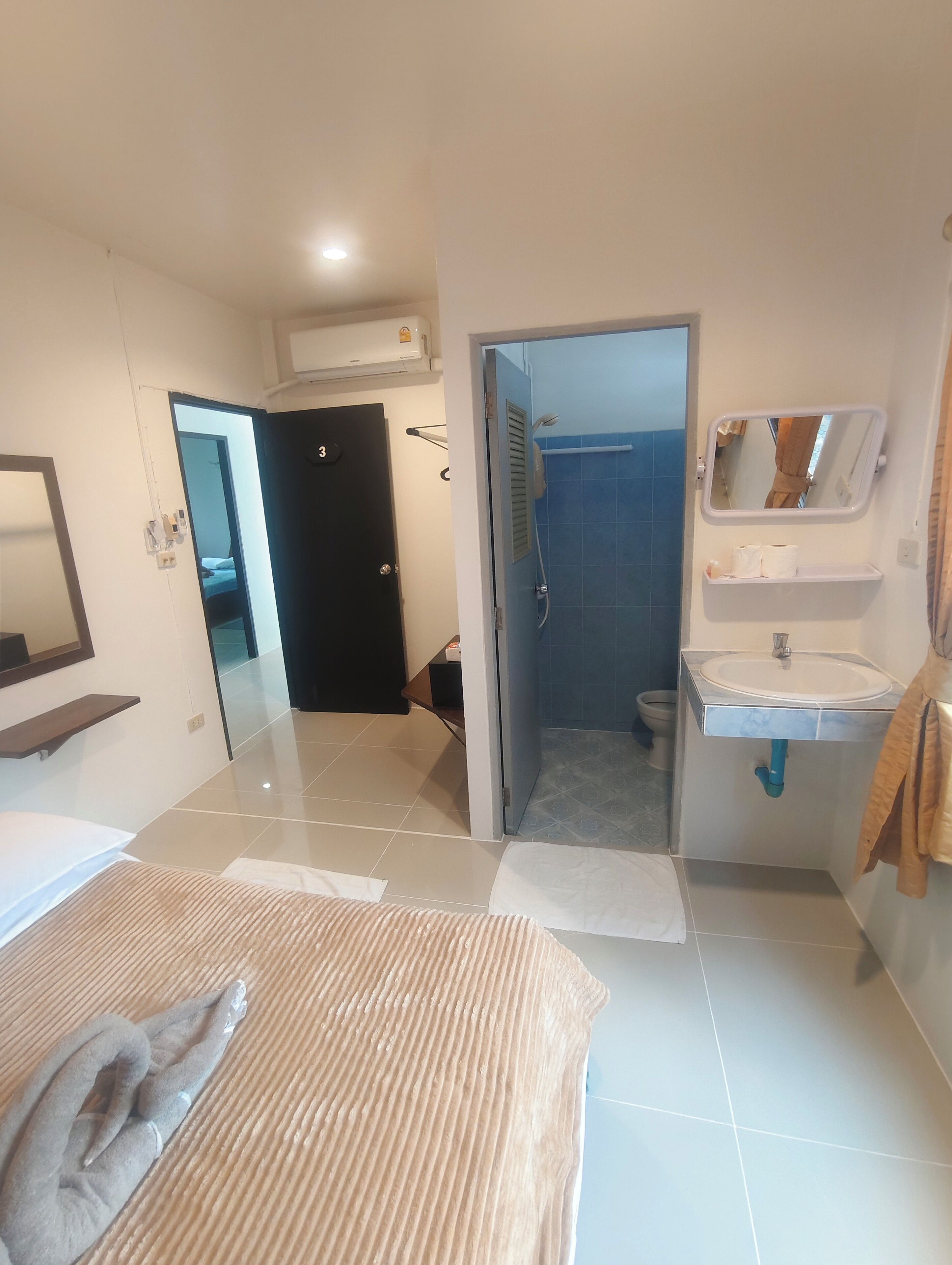 A hotel room with a bed, a bathroom with a shower, a sink, and a mirror.
