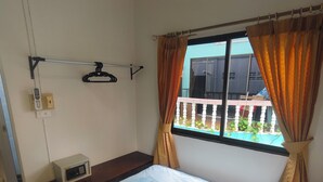 Una camera d'hotel con un letto, un comodino, una finestra con tende, un telefono fissato al muro e vista sul balcone esterno.