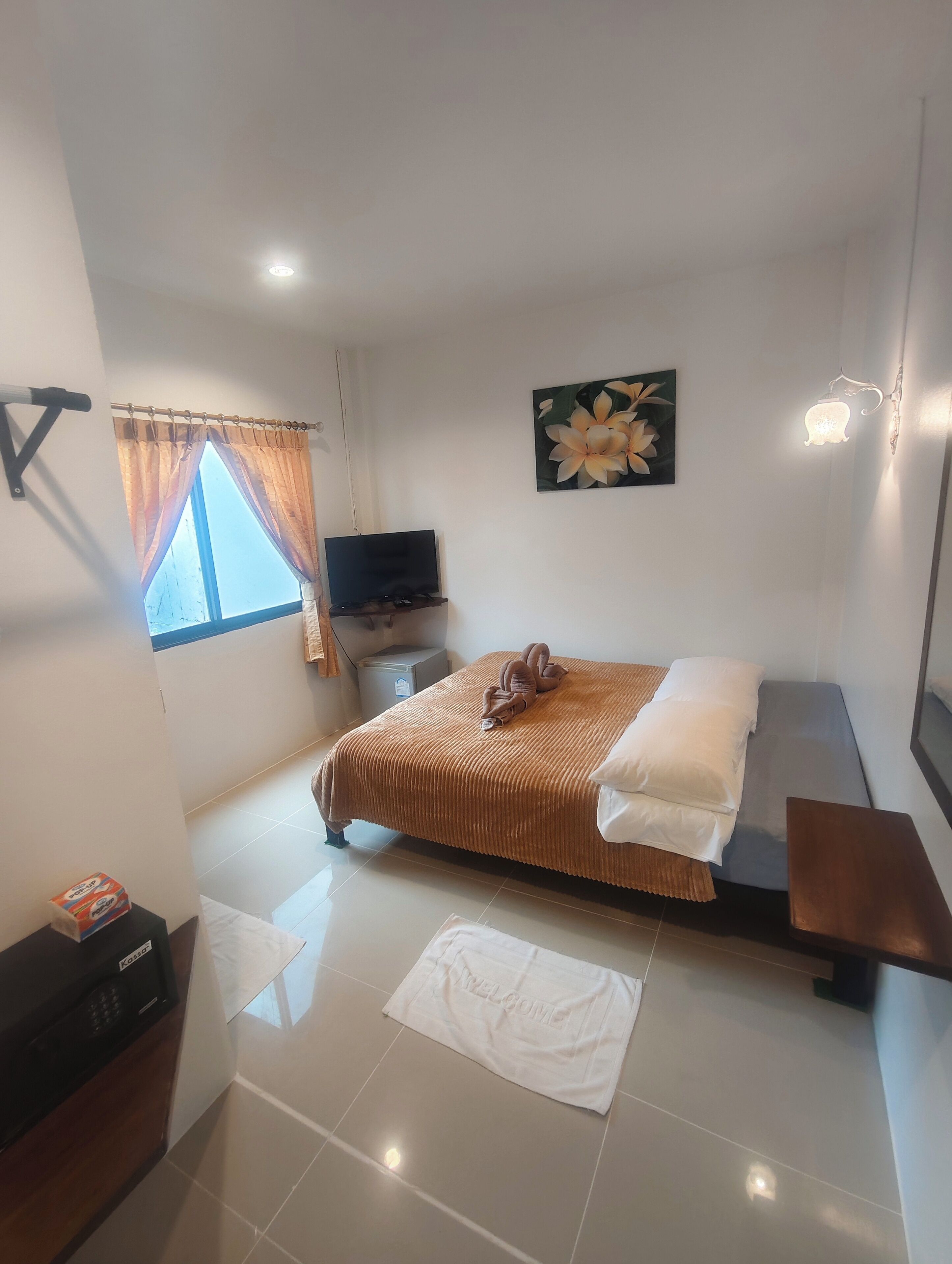 A hotel room with a bed, a TV, a window with curtains, a painting, and a bedside table.