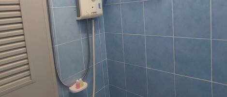 A bathroom with a shower, blue tiles, a white door, and a handrail.