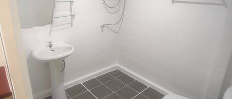 A small bathroom with a white sink, a toilet, and a shower unit.