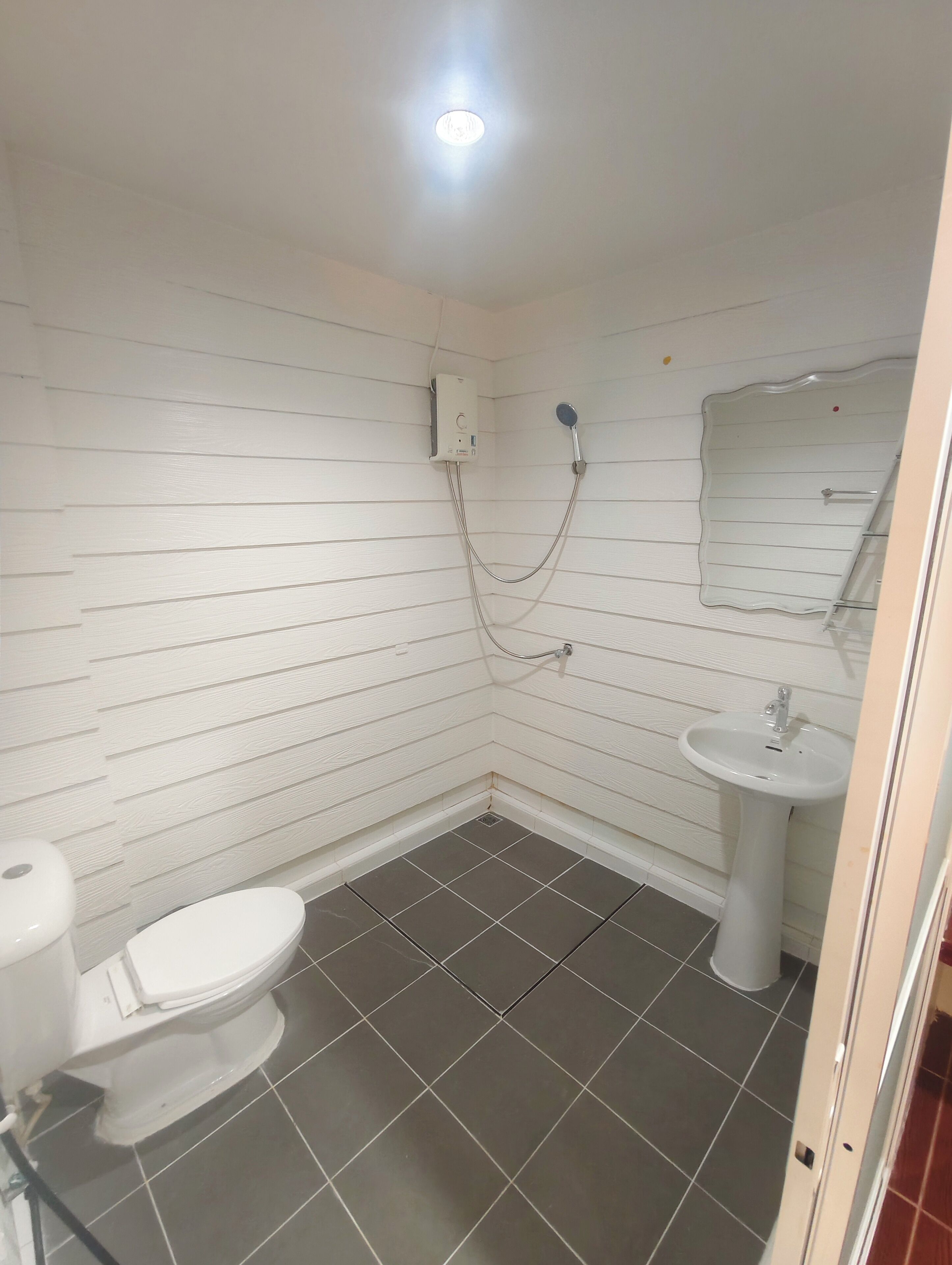 Et lille badeværelse med lyse paneler, toilet, vask og brusebad.