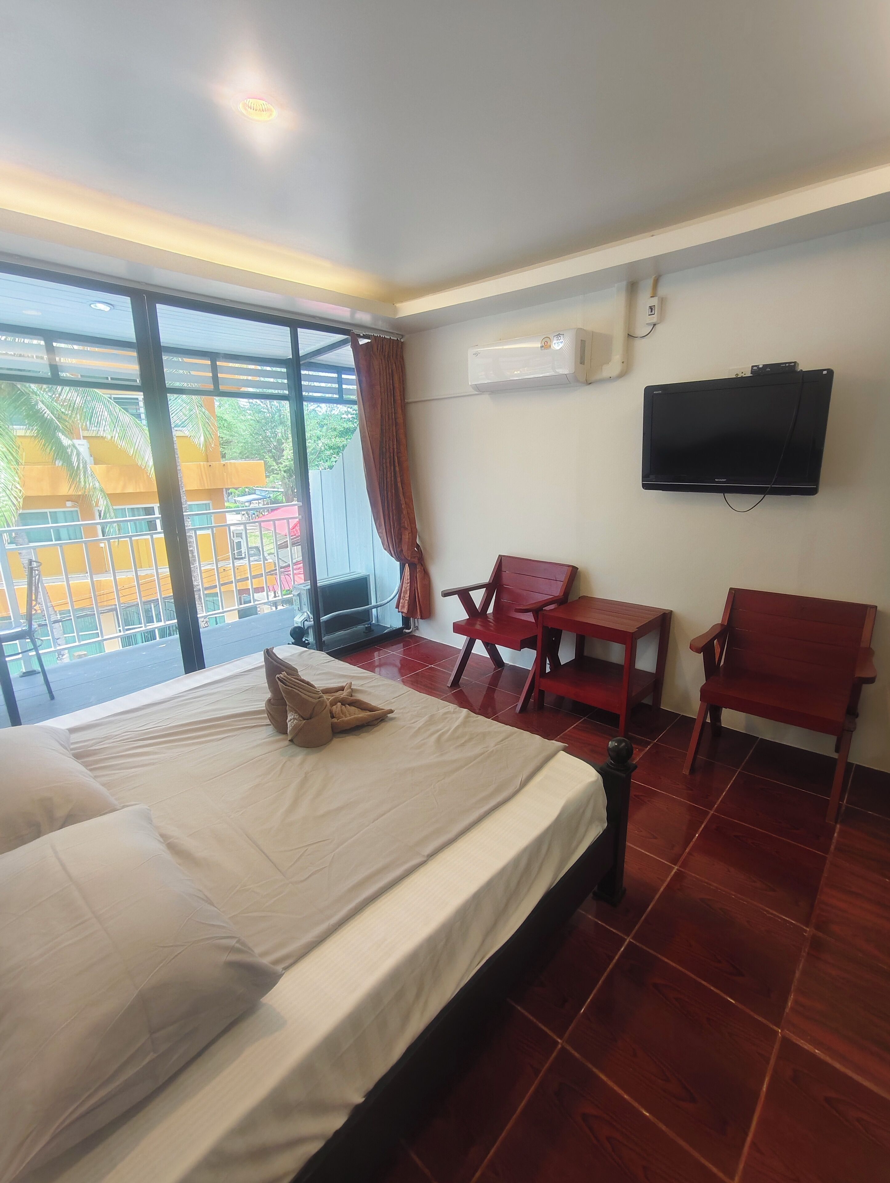 A hotel room with a bed, two chairs, a small table, an air conditioning unit, and a TV mounted on the wall.